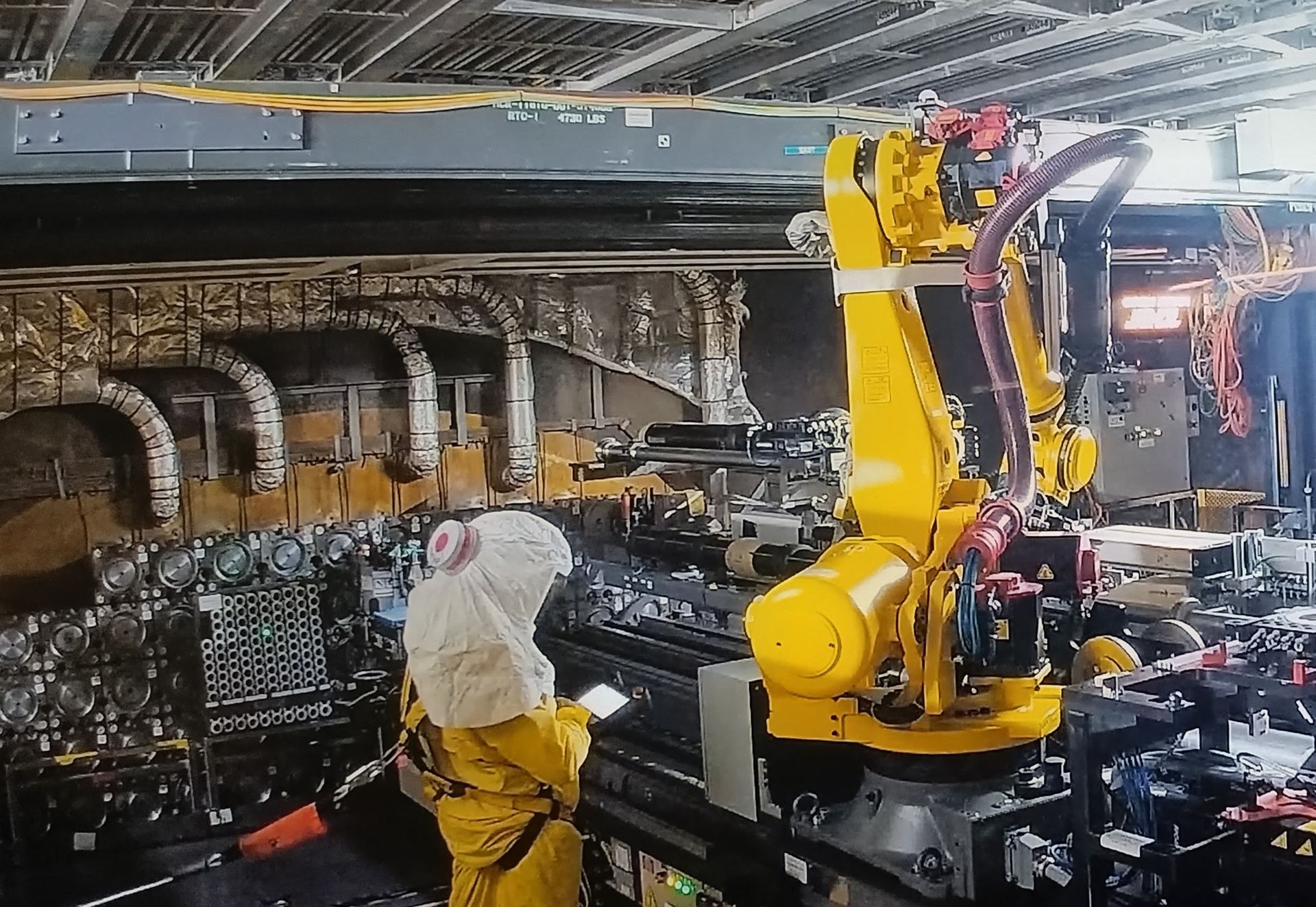 Technician in a protective suit supervising a yellow FANUC robot in an industrial nuclear facility